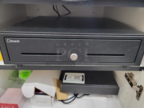 Toast POS cash drawer in black with a keyhole and slot, showing slight wear. Ideal for restaurants or cafes.