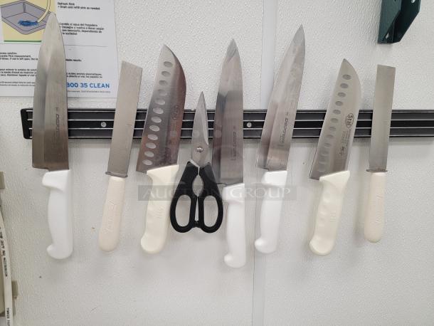 Professional kitchen knives set on magnetic strip, includes various sizes, stainless steel blades, white handles, and scissors.