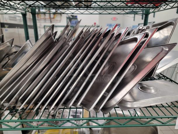 Bulk lot of stainless steel food pans and lids in various sizes on a green Metro rack, ideal for commercial kitchens.