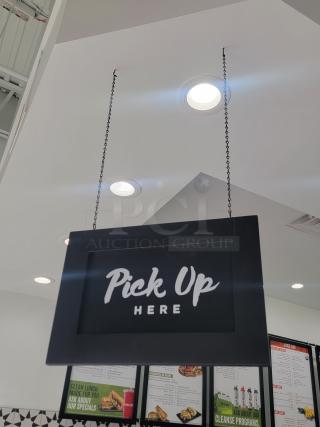 Modern hanging sign reading "Pick Up Here" in white text. Ideal for retail service areas. Black frame, chain-mounted.