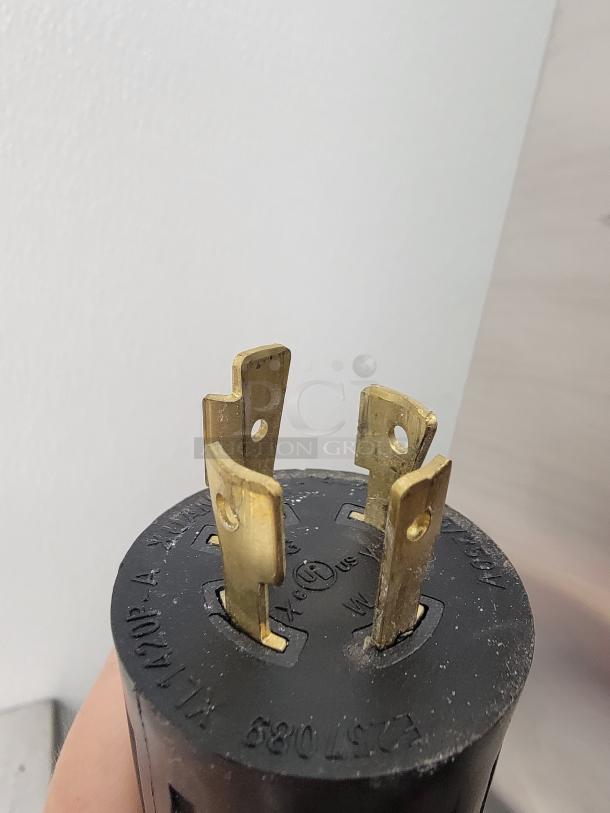 Close-up of a black electrical plug with brass prongs, featuring UL certification markings on surface.
