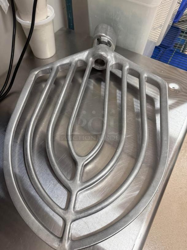 Hobart 1410 mixer paddle attachment, metal design, placed on a stainless steel surface, like new condition.