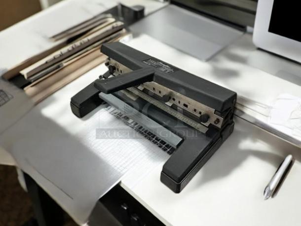 Swingline SWI450 heavy-duty hole puncher in great condition, black metal, with adjustable paper guide, on a white desk.