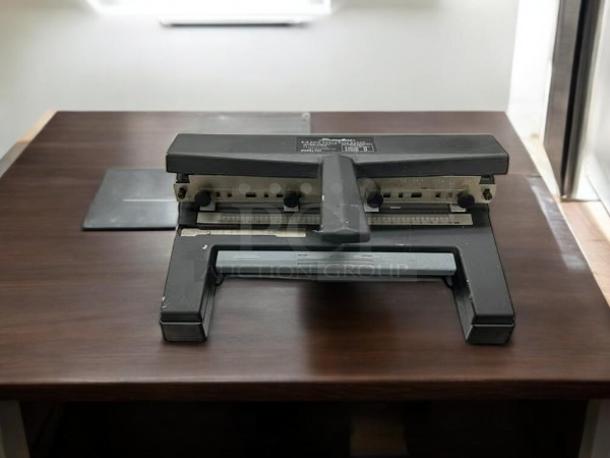 Swingline SWI450 hole punch in great condition on a wooden desk. Black metal finish, adjustable paper guide, visible markings.
