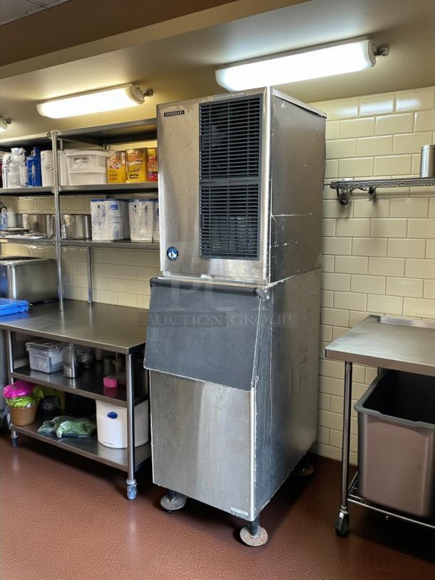 Commercial ice machine with stainless steel finish, ducted grill, and storage bin in a kitchen setting. Wear visible on surface.