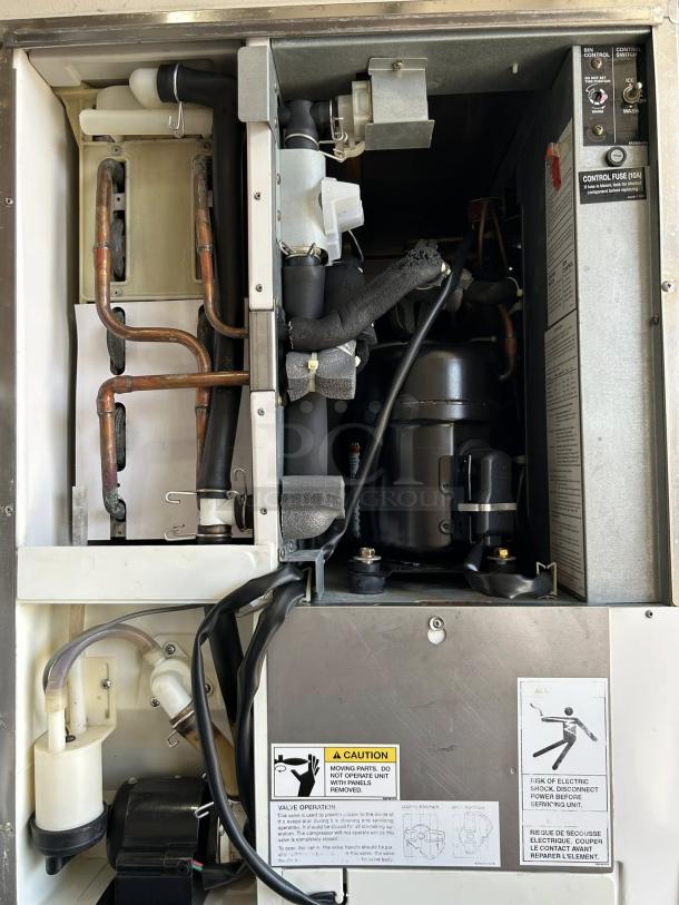 Industrial machine interior with copper and plastic tubing, control panel, black wiring, and caution labels visible.