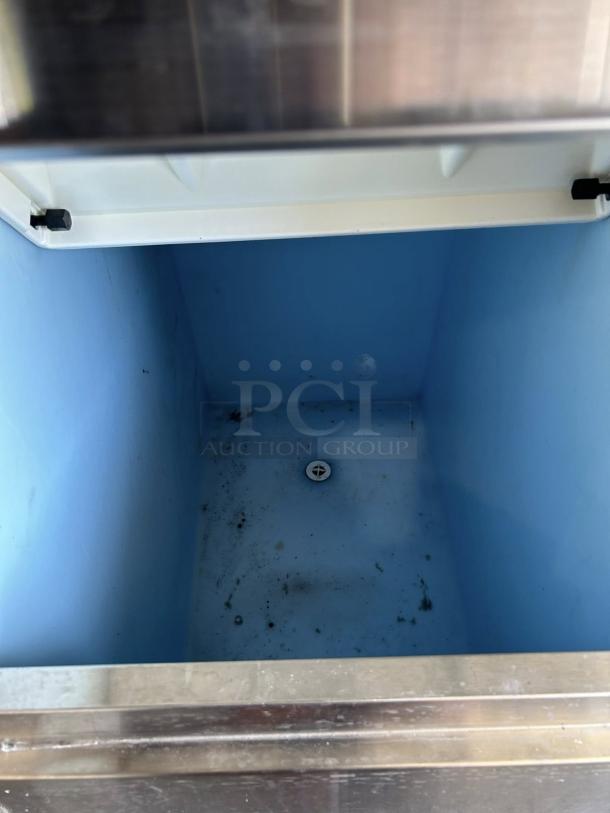 Stainless steel ice storage bin with a blue interior. The bin shows signs of use with visible residue on the bottom.