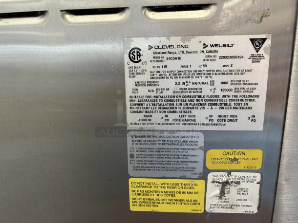 Alt text: "Cleveland Range 24CGA10.2 SteamCraft Gemini Pressureless Convection Gas Steamer, double stacked, 10 pan capacity, 115v. Tags indicate model and safety instructions."