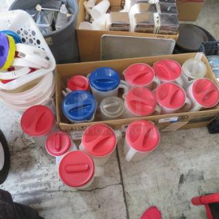 A collection of assorted plastic pitchers with red and blue lids, various sizes, in good condition, stacked in a box.