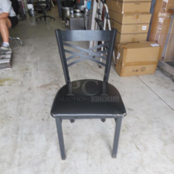 Black metal chair with black cushioned seat, featuring a cross-back design. Shows mild wear, suitable for indoor use.