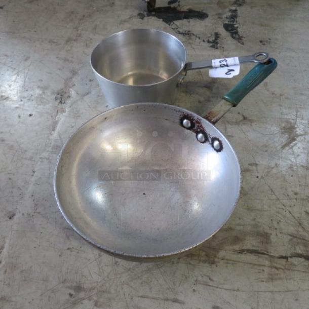 Two assorted metal pans, one with a green handle. Slightly worn. Auction lot tag "2XBID" visible on handle.