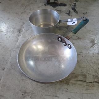 Two assorted metal pans, one with a green handle. Slightly worn. Auction lot tag "2XBID" visible on handle.
