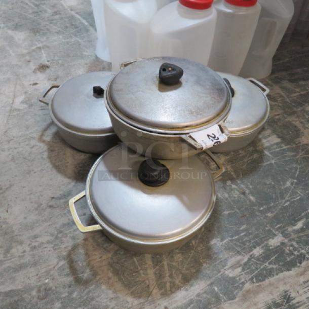 Four aluminum sauce pans with matching lids and side handles, stacked. Includes visible auction tag "4XBID." Well-used condition.