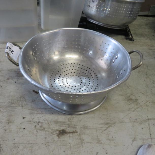 15-inch aluminum colander with dual handles, perforated for draining. Slight wear visible; ideal for kitchen use.