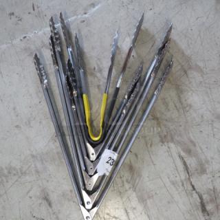 Assorted stainless steel tongs with yellow handles, multiple pieces. Good condition. Tag reads "23".
