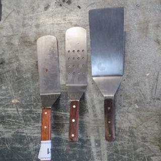 Assorted hamburger turners with wooden handles; includes solid, slotted, and perforated designs. Used condition.