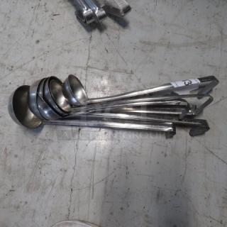 Assorted stainless steel ladles in various sizes, used condition, laid out on the floor. Ladles show standard wear.