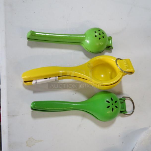 Two green and one yellow citrus press tools on a white surface, showing minor wear, used for extracting juice from fruits.