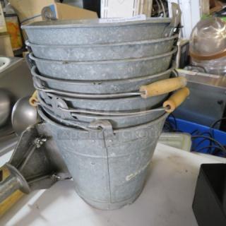 Stack of aluminum beer buckets with wooden handles, visible wear, marked "3XBID," suitable for venue use or decor.