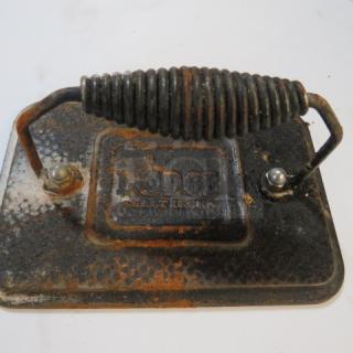 Lodge cast iron steak weight with coiled handle, visible rust, and Lodge logo embossed; used condition.