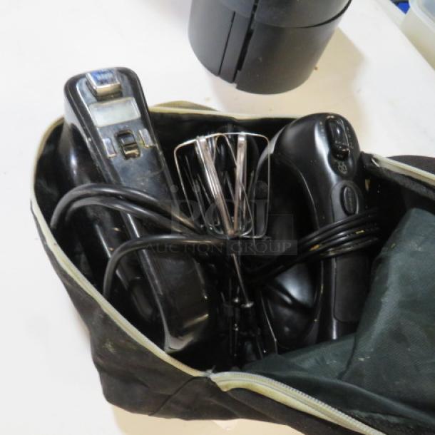 One lot of Oster hand mixers in a zippered black bag; includes two black mixers with attached cords and metal beaters, good condition.