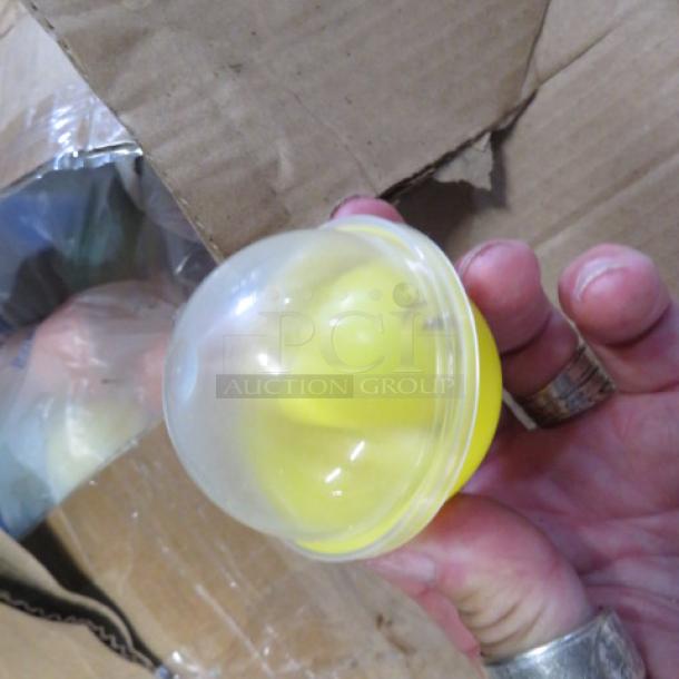Two boxes of vending machine prizes, featuring assorted plastic capsules, some visible with yellow items inside. Cardboard boxes slightly worn.