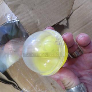 Two boxes of vending machine prizes, featuring assorted plastic capsules, some visible with yellow items inside. Cardboard boxes slightly worn.