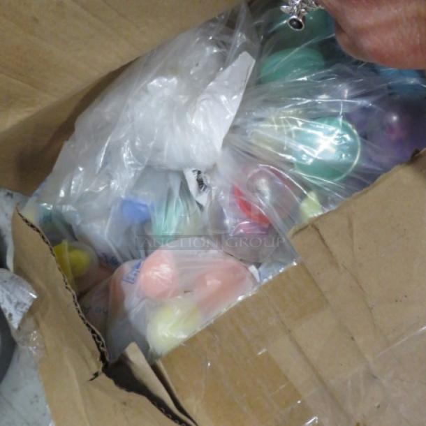 Two boxes of assorted vending machine prizes, various colors, sealed in clear plastic bags.