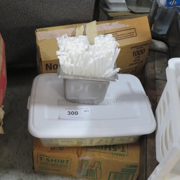 Box containing miscellaneous items, including a metal container with white straws, placed on a plastic lid. Quantity tag shows "300."