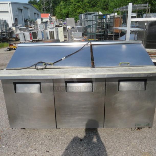 True TSSU-72 refrigerated prep table with three doors, cutting board, and two racks on casters. Industrial-grade stainless steel.