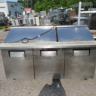 True TSSU-72 refrigerated prep table with three doors, cutting board, and two racks on casters. Industrial-grade stainless steel.