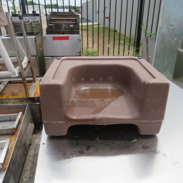 Brown Cambro booster seat with a contoured design, shown outdoors on a metal surface, in good condition.