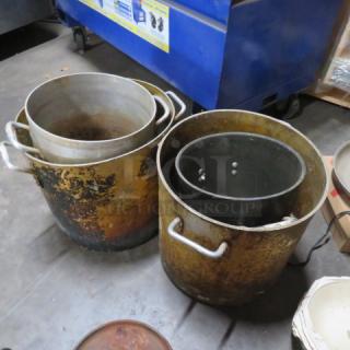 Assorted large stock pots, varying sizes, well-used with visible wear and patina, metal handles, suitable for high-volume cooking.