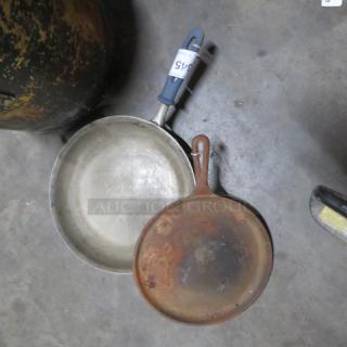 Assorted skillets; one metal with rubber handle, one rusted cast iron. Visible tag reads "2XBID". Condition varies.