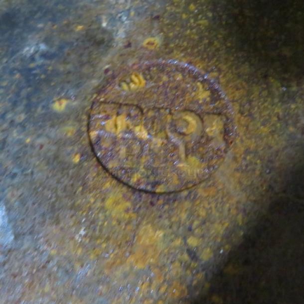 Engraved skillet bottom with circular logo, showing wear and rust, indicative of vintage condition.