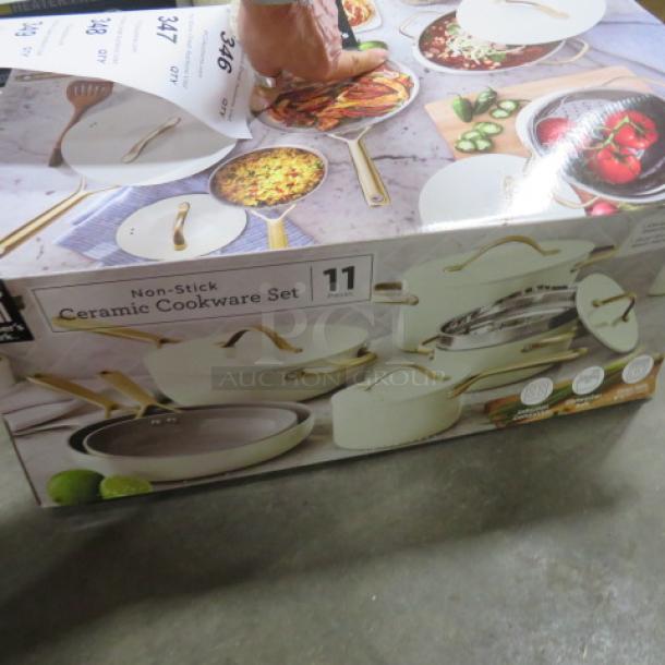11-piece non-stick ceramic cookware set in box. Features gold handles, includes various pots and pans. New condition.