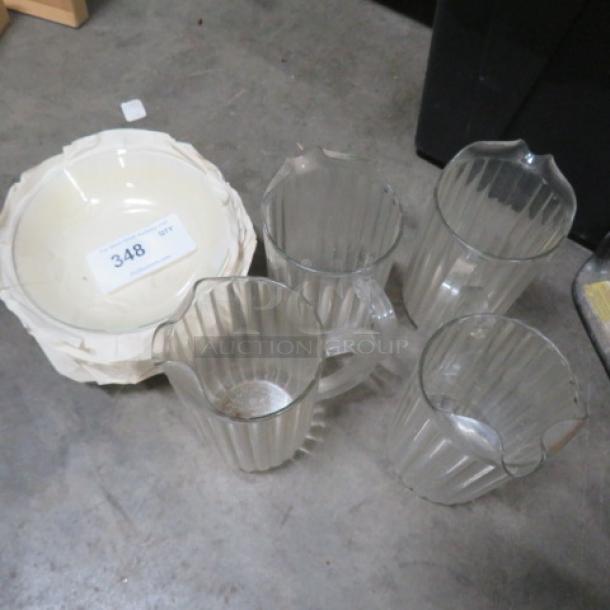 Set of four clear glass pitchers with ribbed design, alongside a white ceramic bowl. Condition appears used. Numbered tag 348 visible on the bowl.