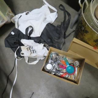 Lot of mixed measuring cups, spoons, and aprons. Includes metal and colored plastic tools, various sizes in used condition.
