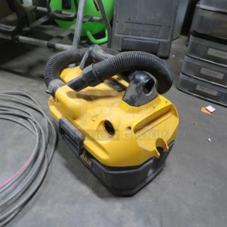 Dewalt shop vac in used condition; yellow and black with attached hose on a concrete floor.