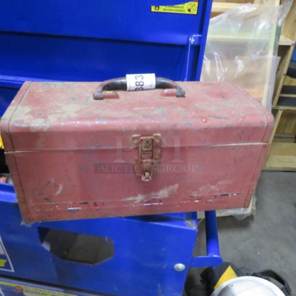 Vintage red metal toolbox with handle and latch; shows signs of wear and rust, indicating age and use.