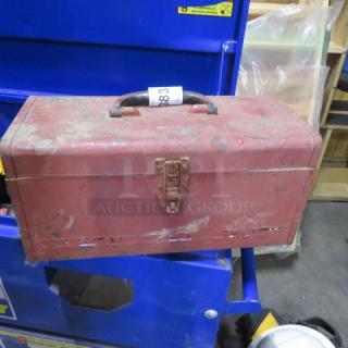 Vintage red metal toolbox with handle and latch; shows signs of wear and rust, indicating age and use.