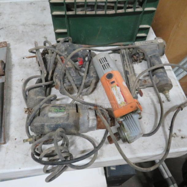 Assorted power tools, including drills and saws, visibly worn with cords tangled, on a table; condition appears used.