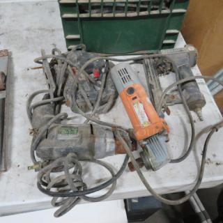 Assorted power tools, including drills and saws, visibly worn with cords tangled, on a table; condition appears used.