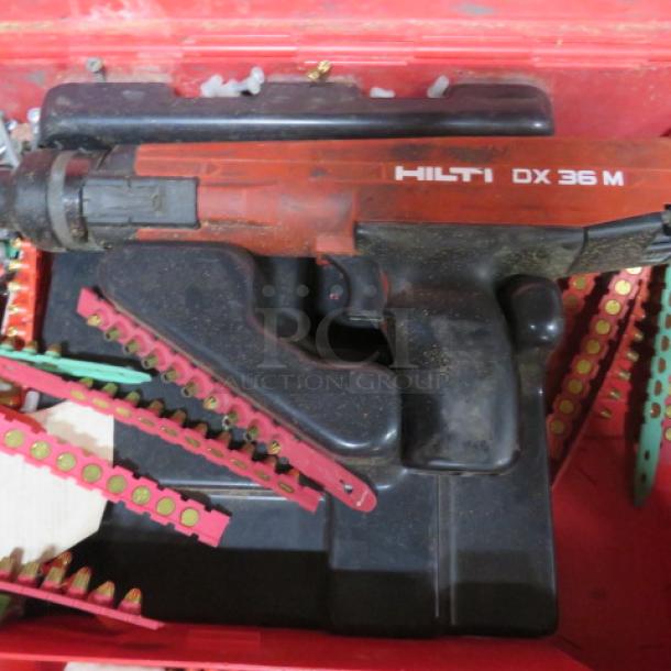 Hilti DX36M fastening tool in red carry case, visible wear, includes fastener strips; ideal for construction tasks.