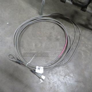 Coiled steel cable tie with looped ends on a concrete floor; tag marked "393" attached. Slight wear visible.