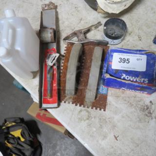 Lot of miscellaneous items on a table, including a plastic jug, metal tools, concrete nails in a Powers box, and a clamp.