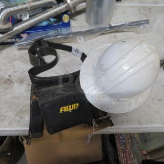 Assorted lot including a white hard hat and AWP tool belt on a table. Visible wear on items. Additional tools in the background.