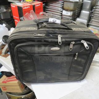 Black Samsonite wheeled bag, used condition, multiple zippered compartments, visible Samsonite logo tag on the front.