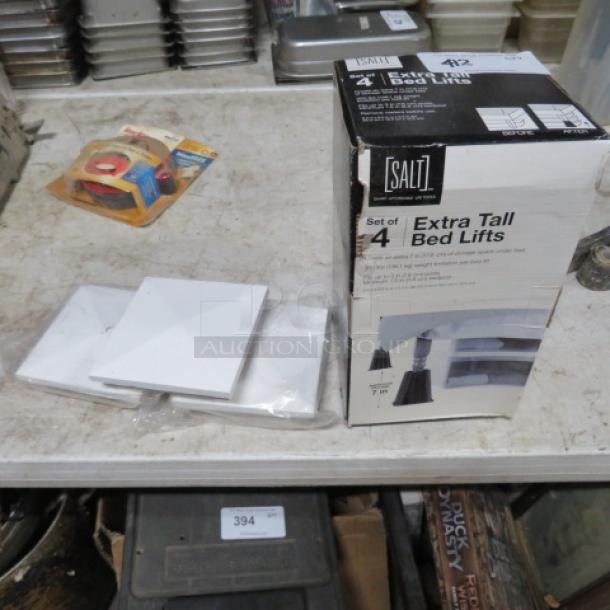 Box of Salt extra tall bed lifts, unopened pack. Miscellaneous items, including adhesive tape rolls and white plastic or ceramic tiles, visible on a table.