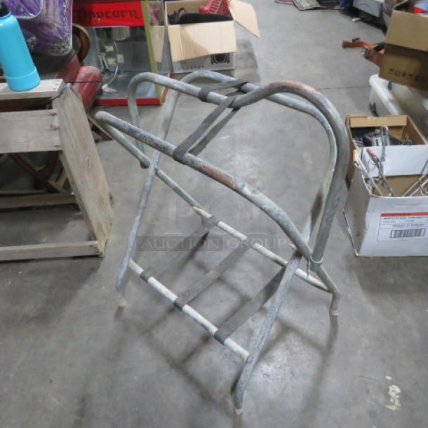 Metal saddle stand, tubular frame, used condition with visible wear and rust, sturdy construction.